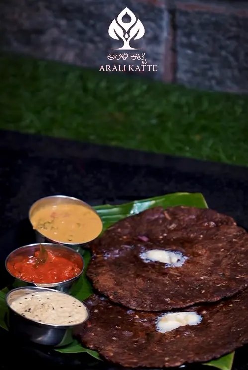 Dark dosa topped with butter, served with sambar and chutneys on a banana leaf