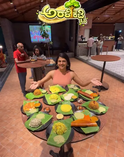 A guest welcoming viewers to a table laid with banana-leaf plates of South Indian dishes