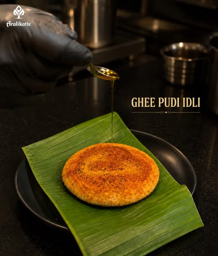 Ghee being drizzled over a ghee pudi idli on a banana leaf